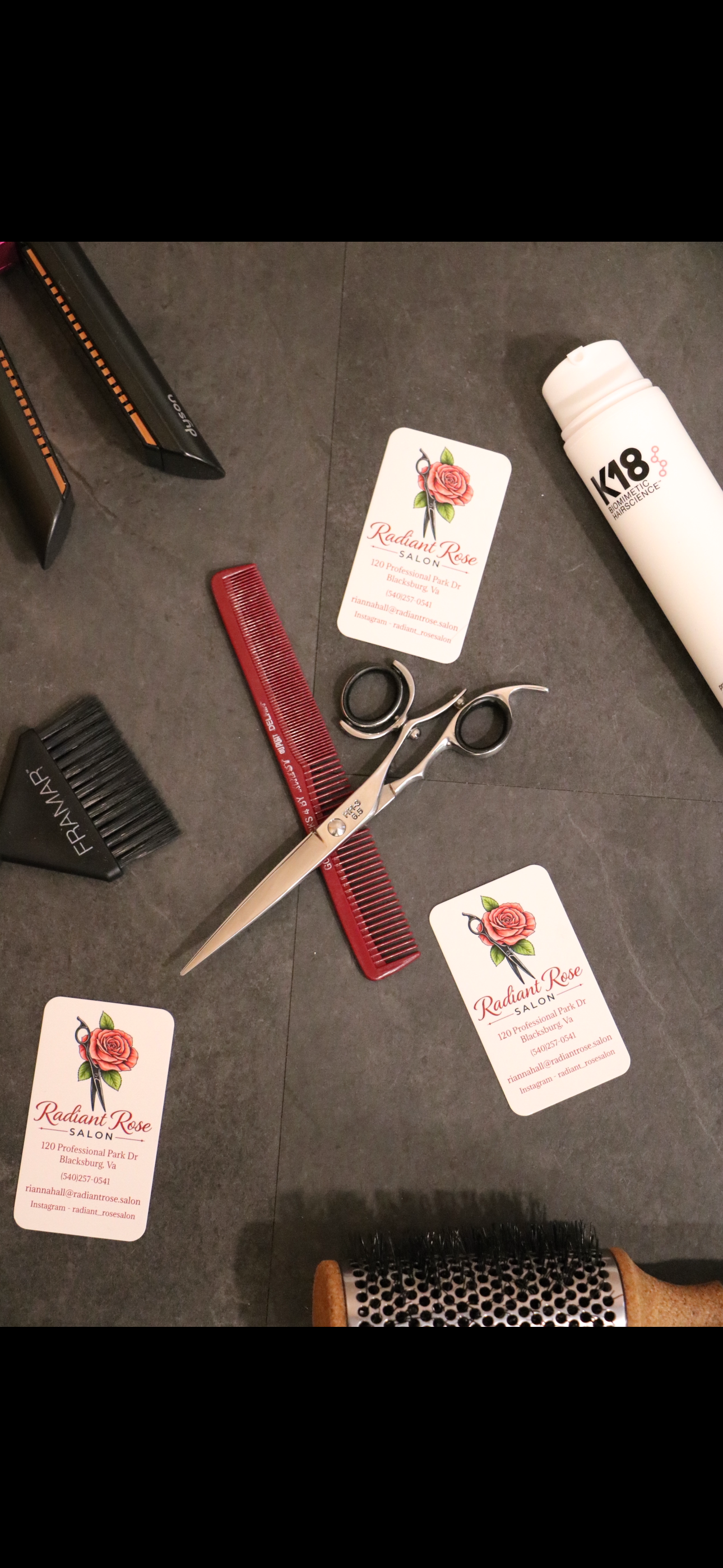 Hair styling tools on a dark surface: combs, scissors, clips, brush, and a spray bottle.