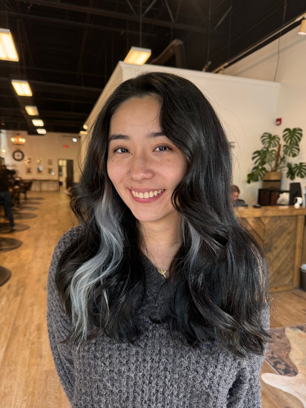 Smiling person with long black hair in a cozy café with warm lighting and wooden tables