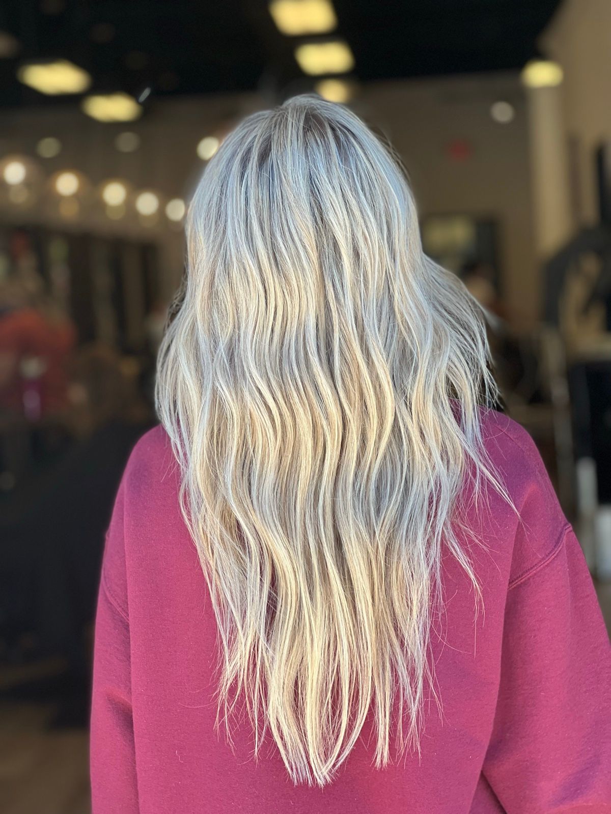 Person with long wavy silver hair wearing a burgundy top, seen from behind indoors.