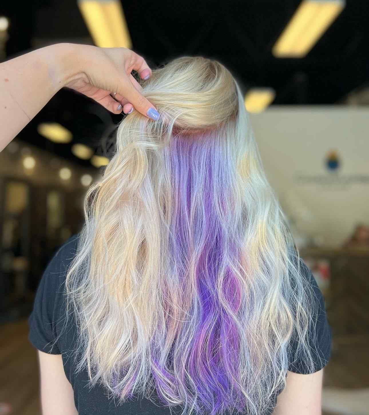 Back view of long blonde hair with pastel purple streaks being lifted by a hand