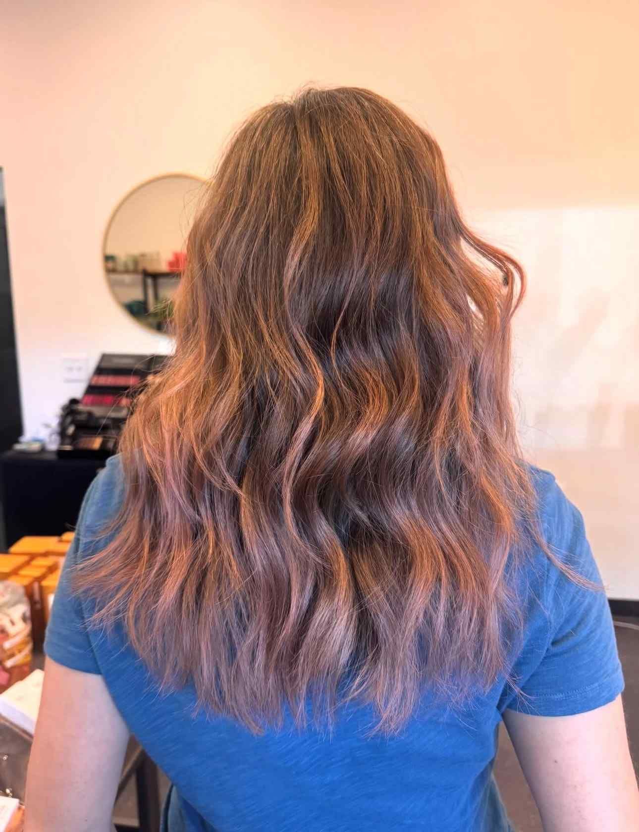 Back view of long wavy brown hair over a blue shirt in a softly lit room