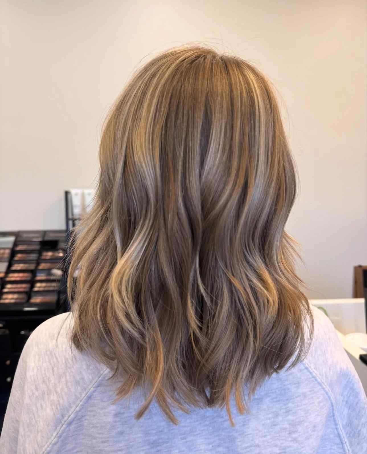 Wavy shoulder-length blonde hair with soft highlights, shown from the back in a salon setting