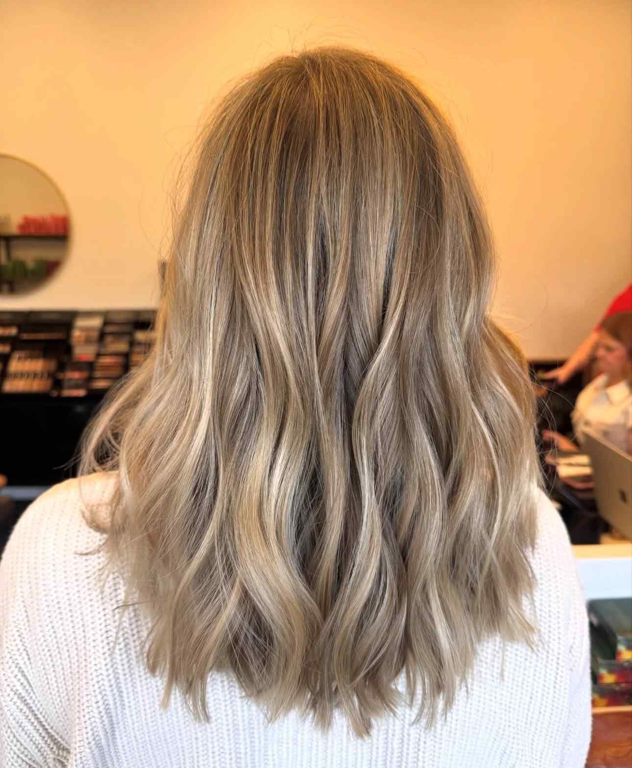 Back view of shoulder-length wavy ash-blonde hair in a salon chair