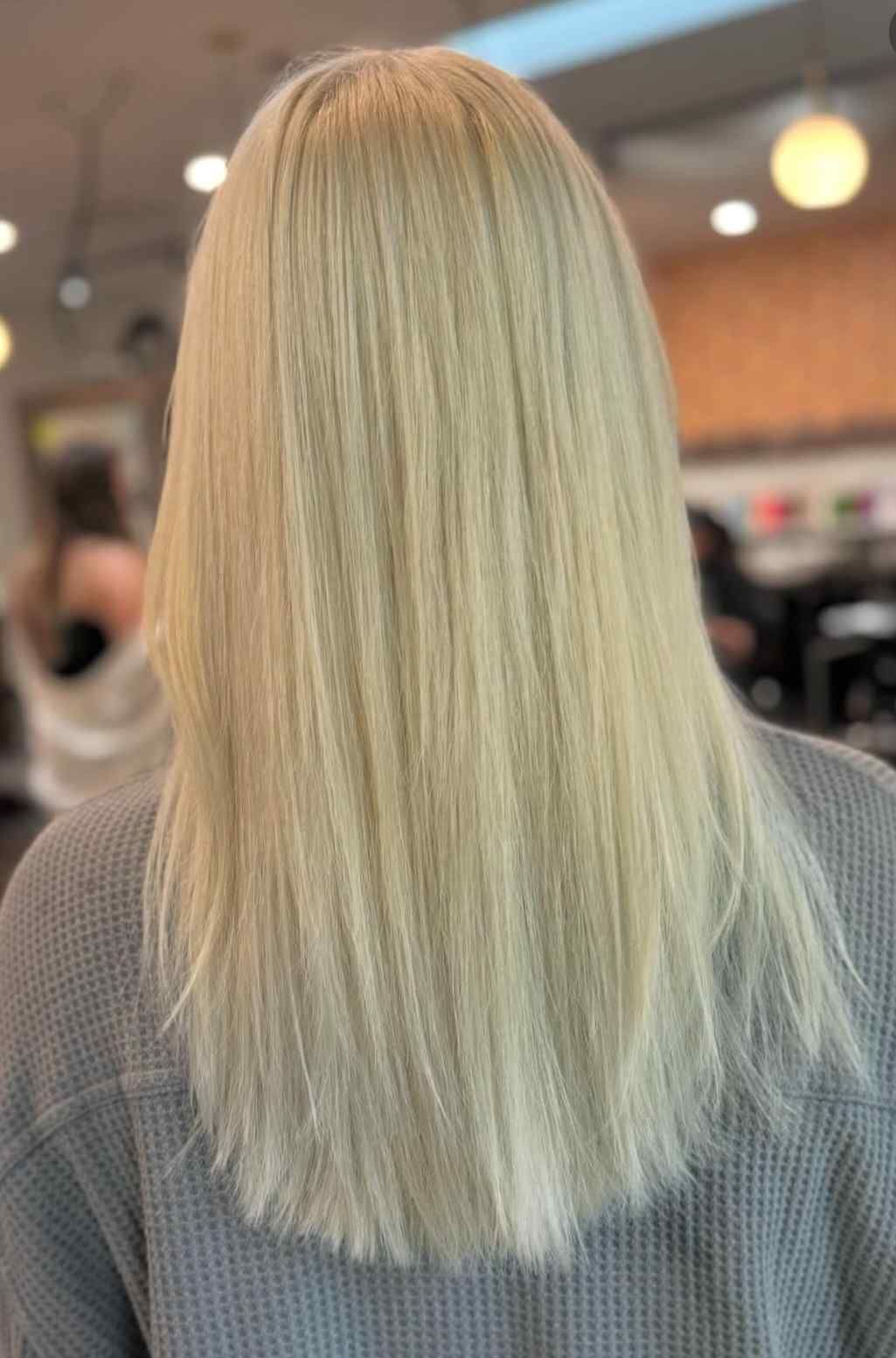 Blonde shoulder-length hair viewed from behind in a salon, with a straight, layered cut.