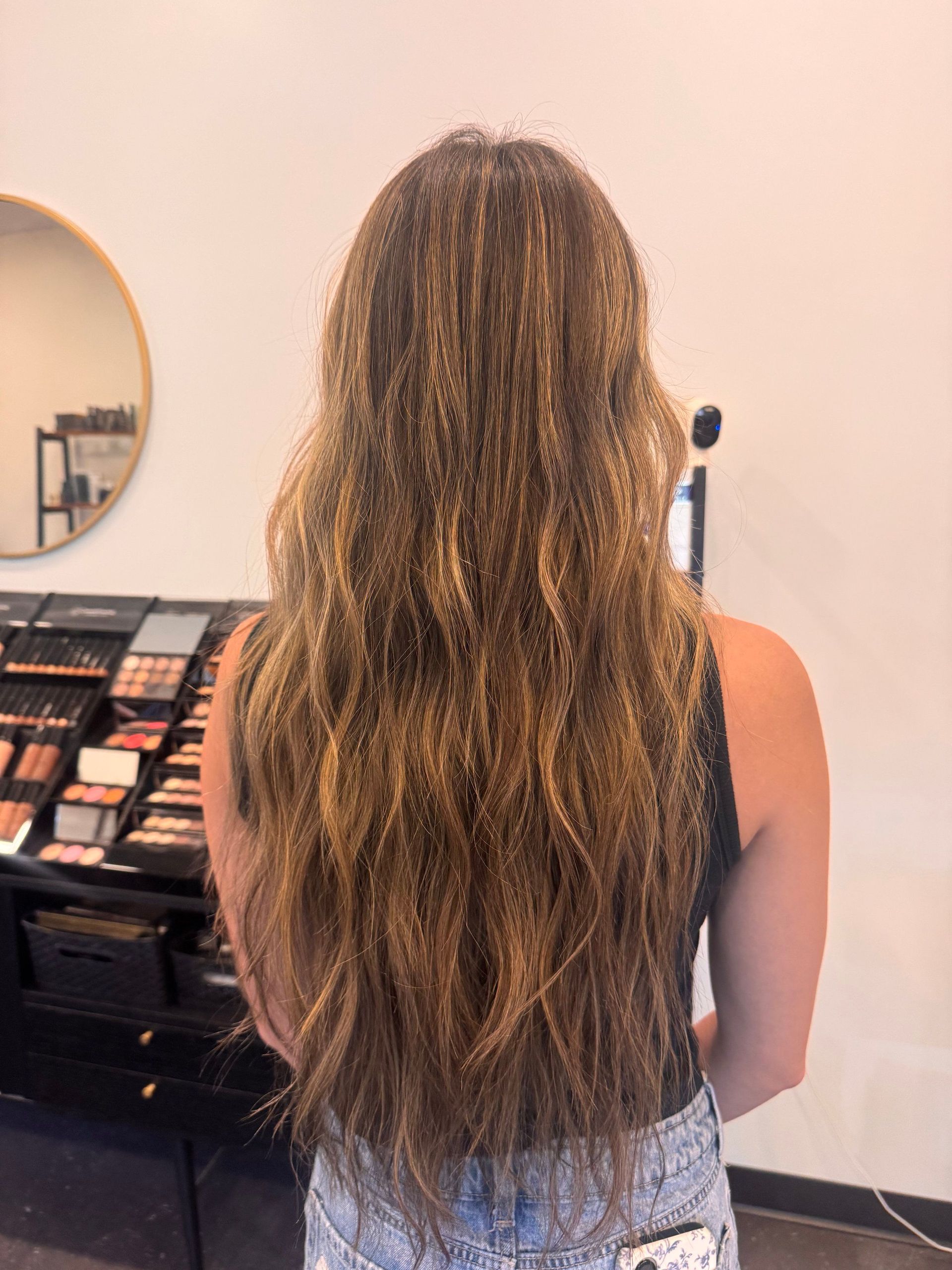 Person with long wavy hair stands in a makeup store, facing a display of cosmetics.