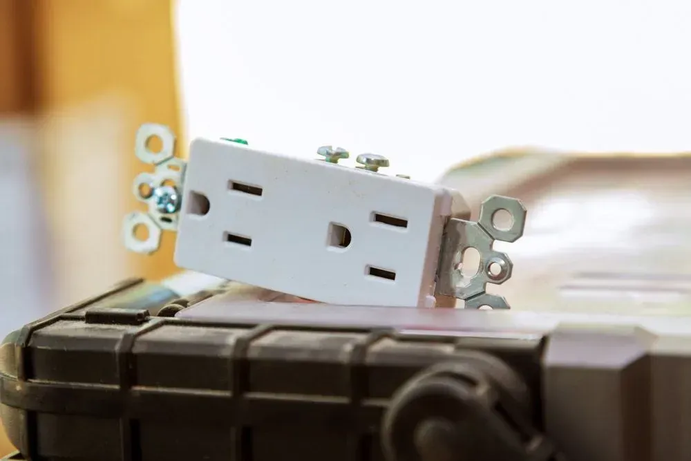 A White, Two-socket Electrical Wall Outlet Resting on a Dark, Textured Utility Box — CH Electrics in Emerald, QLD