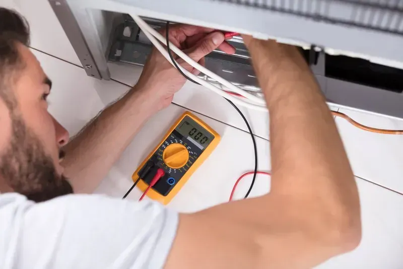 A Technician Testing Wires Inside an Appliance With a Yellow Digital Multimeter — CH Electrics in Emerald, QLD