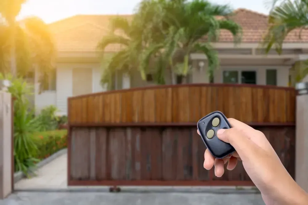 A Hand Holds a Remote Control Toward a Wooden Gate in Front of a House — CH Electrics in Emerald, QLD