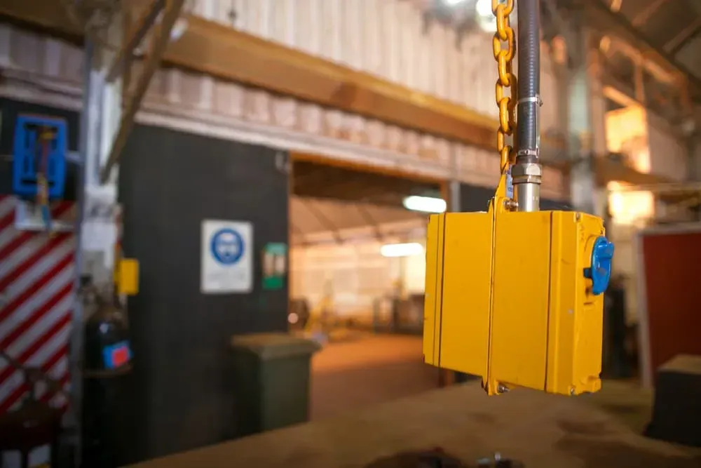 A Yellow Industrial Crane Pendant Control Hanging From a Chain Inside a Workshop — CH Electrics in Emerald, QLD