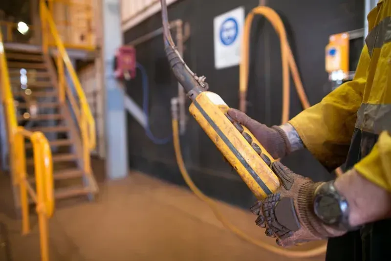 A Person in a Yellow Safety Uniform Holds a Yellow Industrial Crane — CH Electrics in Emerald, QLD