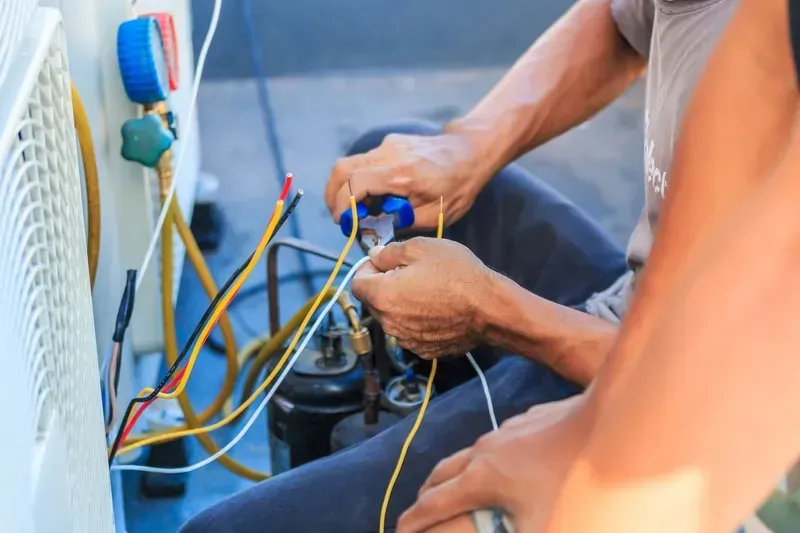Technician Repairing an Outdoor Air Conditioning Unit by Stripping Wires — CH Electrics in Emerald, QLD