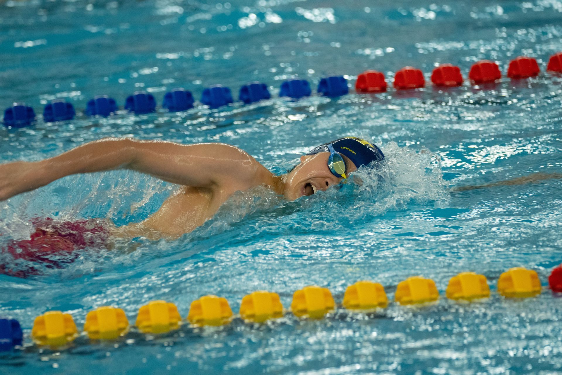 Swimmer doing freestyle in a lane of a pool with blue, red, and yellow lane markers