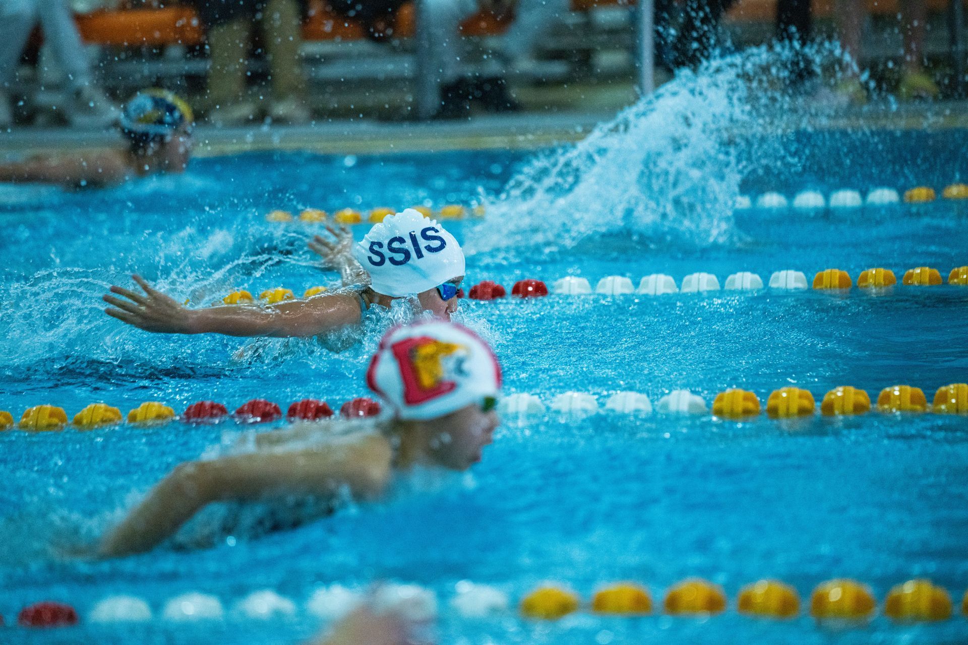 Swimmers racing in a pool, with splashing water and lane markers visible