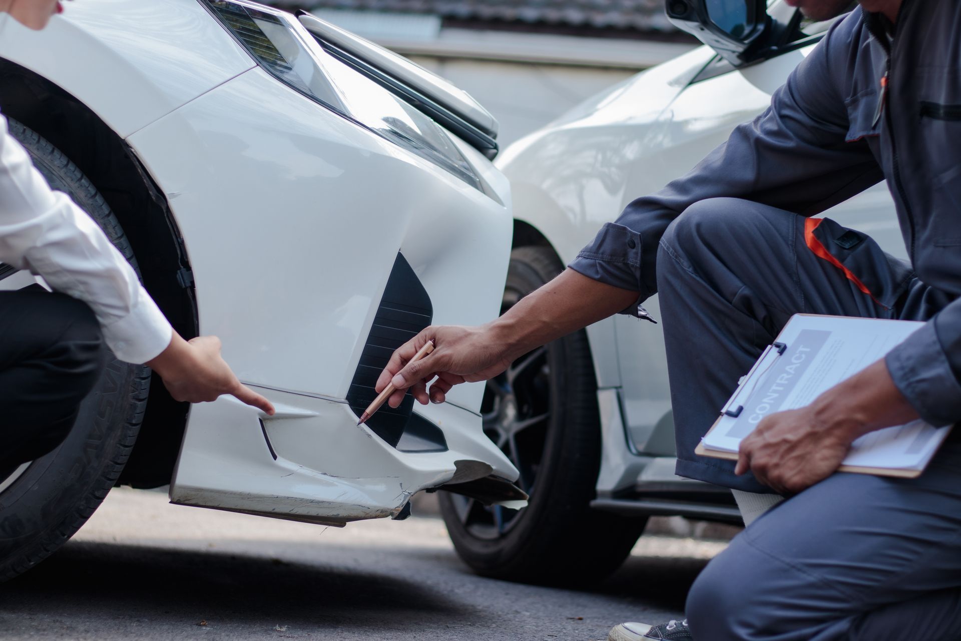 Two people inspect damage on the rear bumper of a white car after a collision.