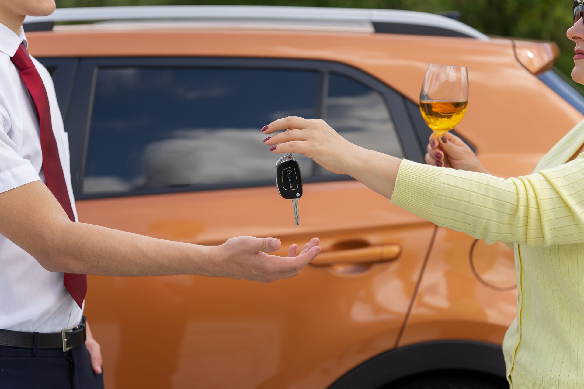 Person handing car keys and a wine glass near an orange SUV, suggesting a designated driver handoff