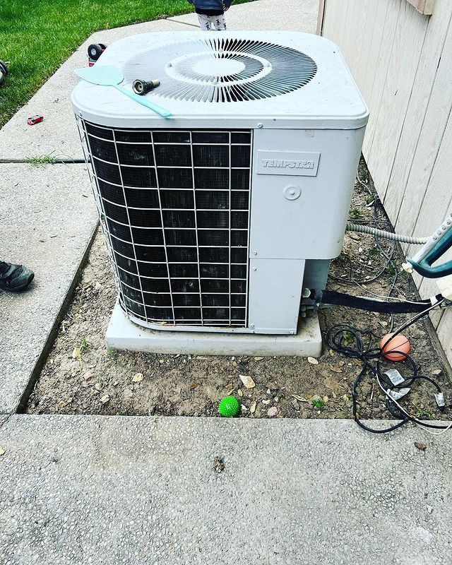 A white air conditioner is sitting in the dirt next to a sidewalk.