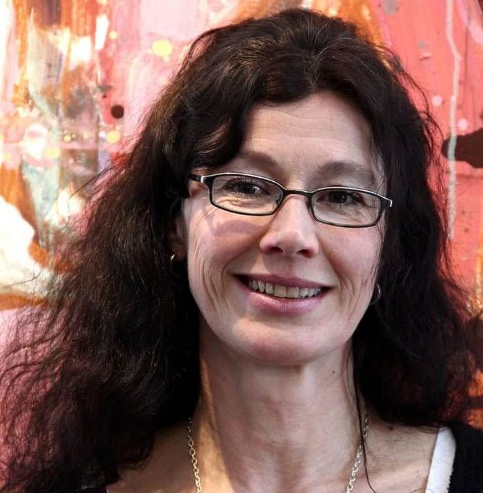 Bilde av Anne-Maria S Håndstad, som smiler foran en rosa bakgrunn.