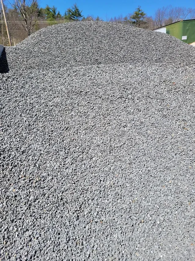 A large, cone-shaped pile of grey crushed gravel sits outdoors under a clear blue sky.