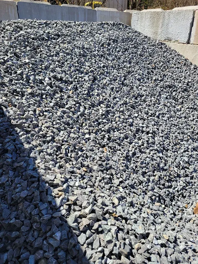 Pile of gray gravel or crushed stone in an outdoor storage area against concrete barriers
