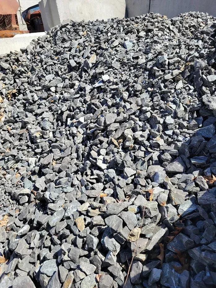 A large, textured pile of dark gray crushed gravel or stones in an outdoor setting.