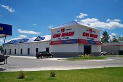 Car dealership building with red signage under a blue sky, with a parked black car in front.