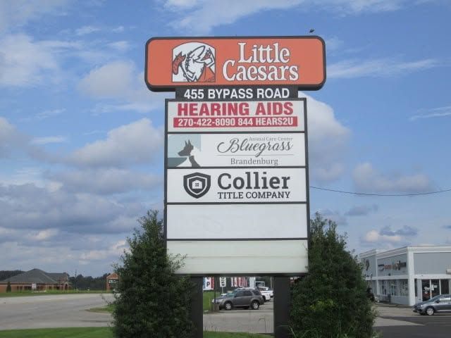 Sign for Little Caesars and nearby businesses beside a road under a cloudy sky. Sign for Little Caesars and nearby businesses beside a road under a cloudy sky.