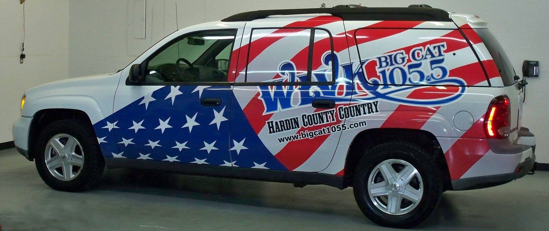 White SUV with an American flag wrap and “WNC” logo parked outdoors. White SUV with an American flag wrap and “WNC” logo parked outdoors.