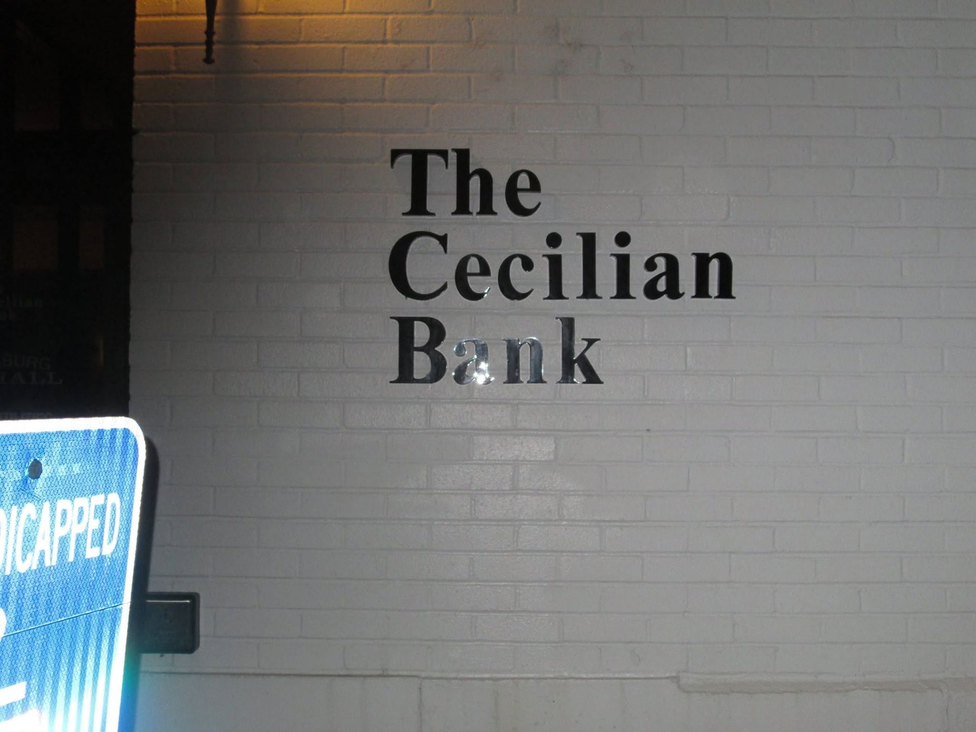 The Cecilian Bank sign on a white brick wall at night. The Cecilian Bank sign on a white brick wall at night.