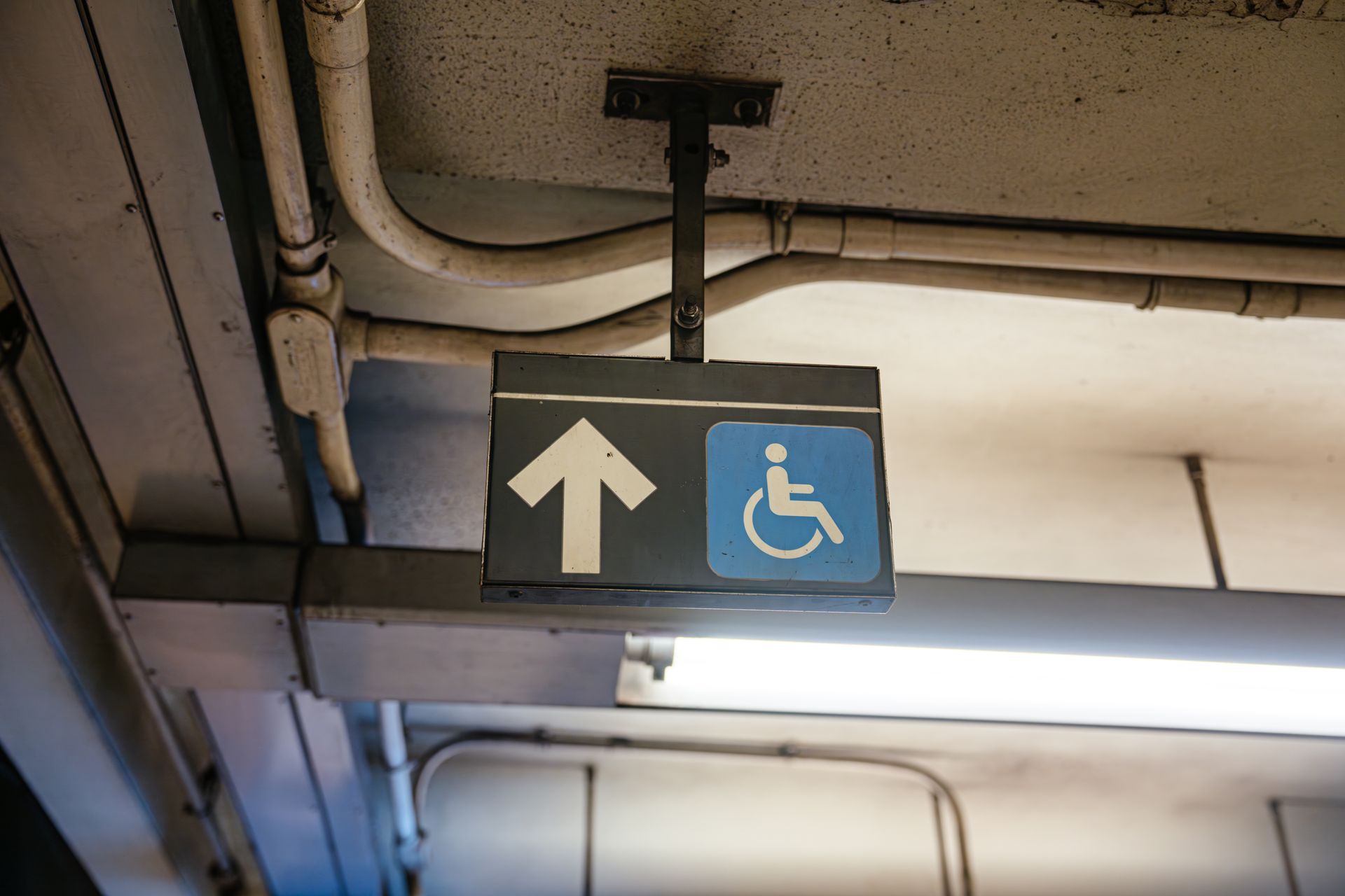 Overhead sign with white up arrow and blue wheelchair accessibility symbol in an indoor corridor. Overhead sign with white up arrow and blue wheelchair accessibility symbol in an indoor corridor.