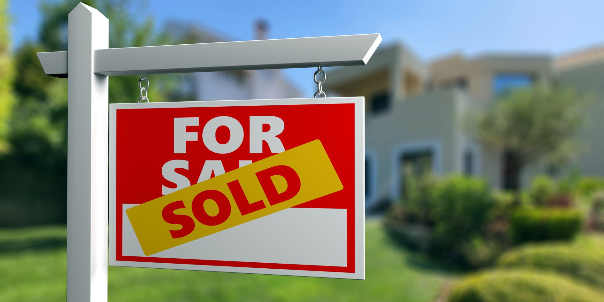 For sale sign on a white post in front of a house, with a yellow sold banner across it. For sale sign on a white post in front of a house, with a yellow sold banner across it.