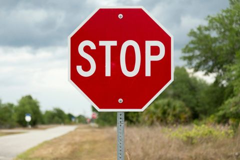 Red stop sign on a rural roadside with trees and cloudy sky in the background.