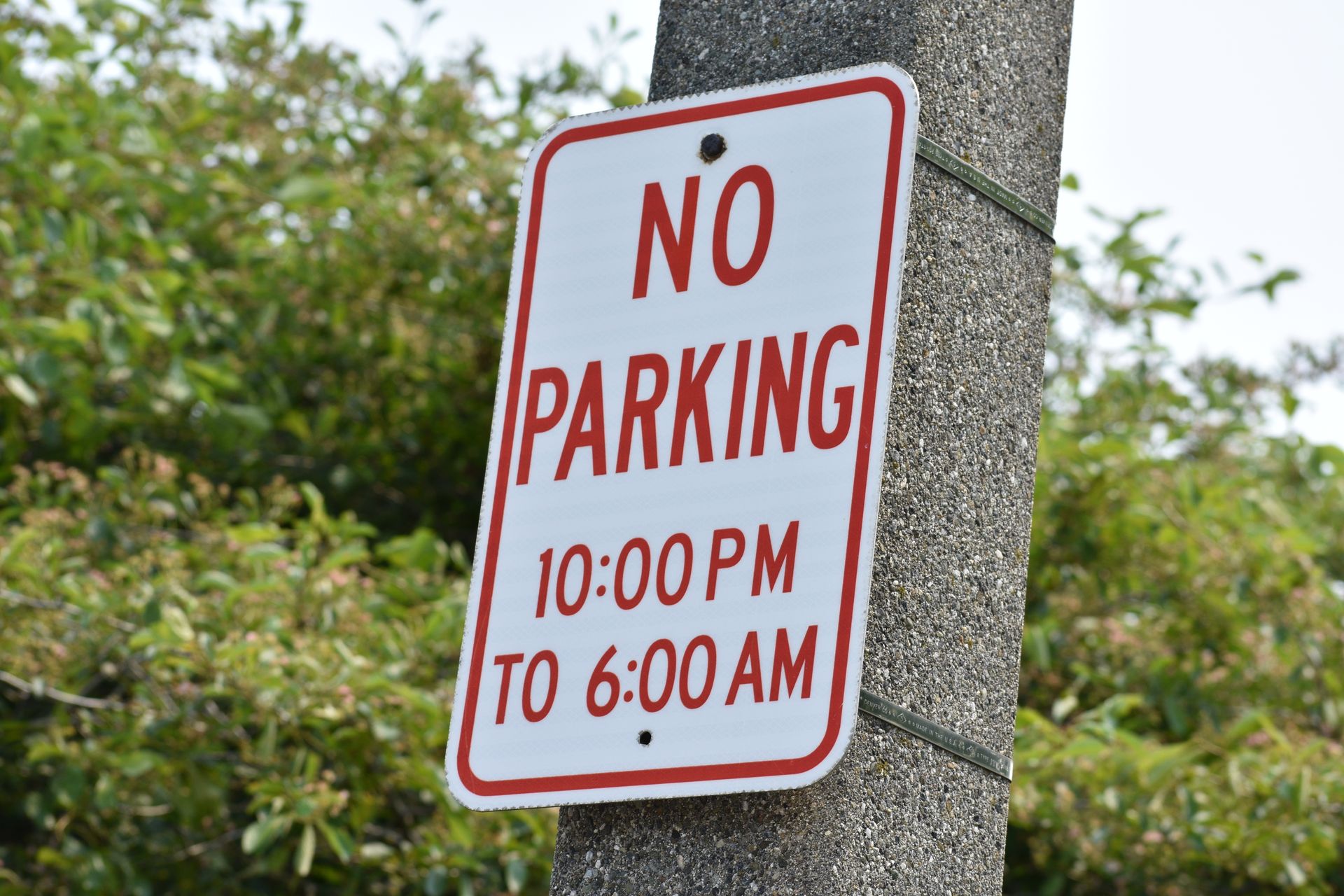 Red-and-white no parking sign on a post, reading 10:00 PM to 6:00 AM. Red-and-white no parking sign on a post, reading 10:00 PM to 6:00 AM.