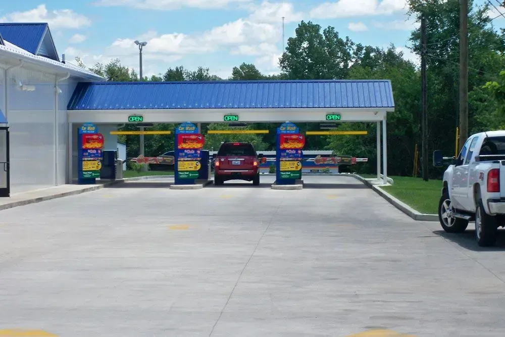 Drive-thru car wash with three bays, colorful signs, and a red car in the center.