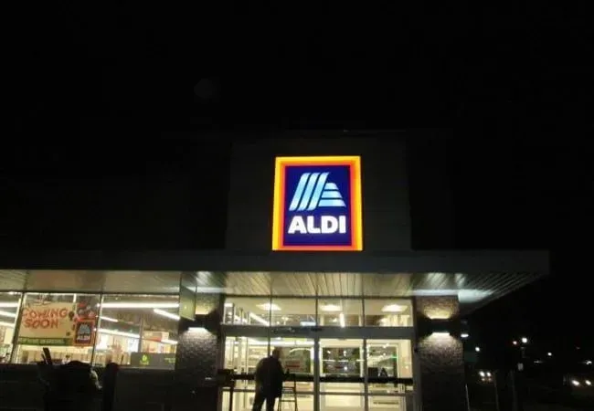 Nighttime exterior of an ALDI store with illuminated entrance and logo sign.