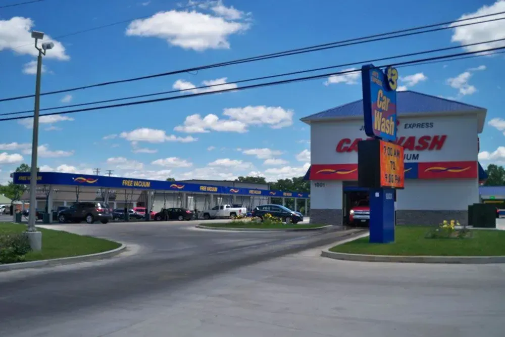 Car wash with blue sign and pumps beside a road under a sunny sky.