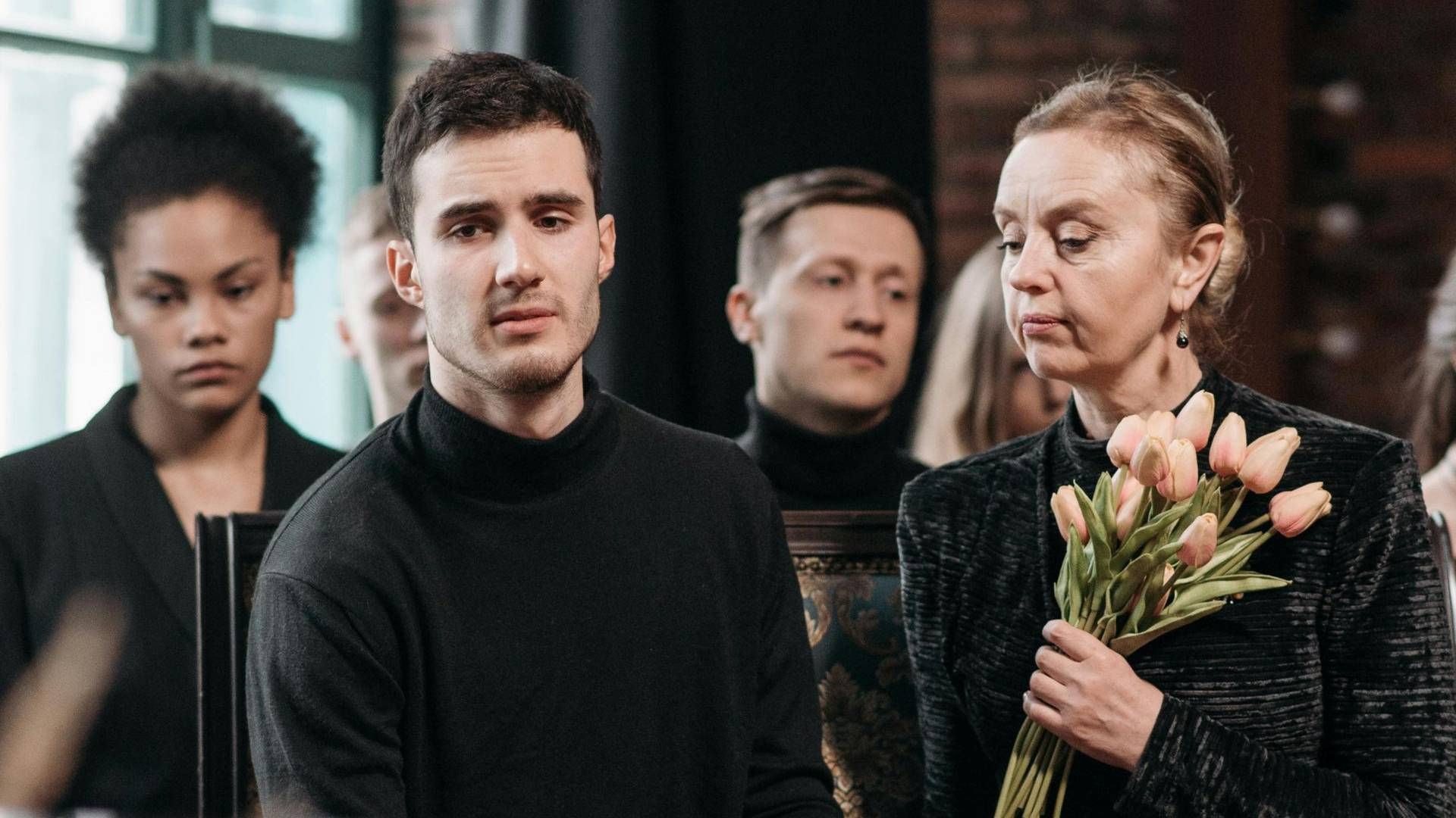Young adult mourners holding flowers together at a funeral service