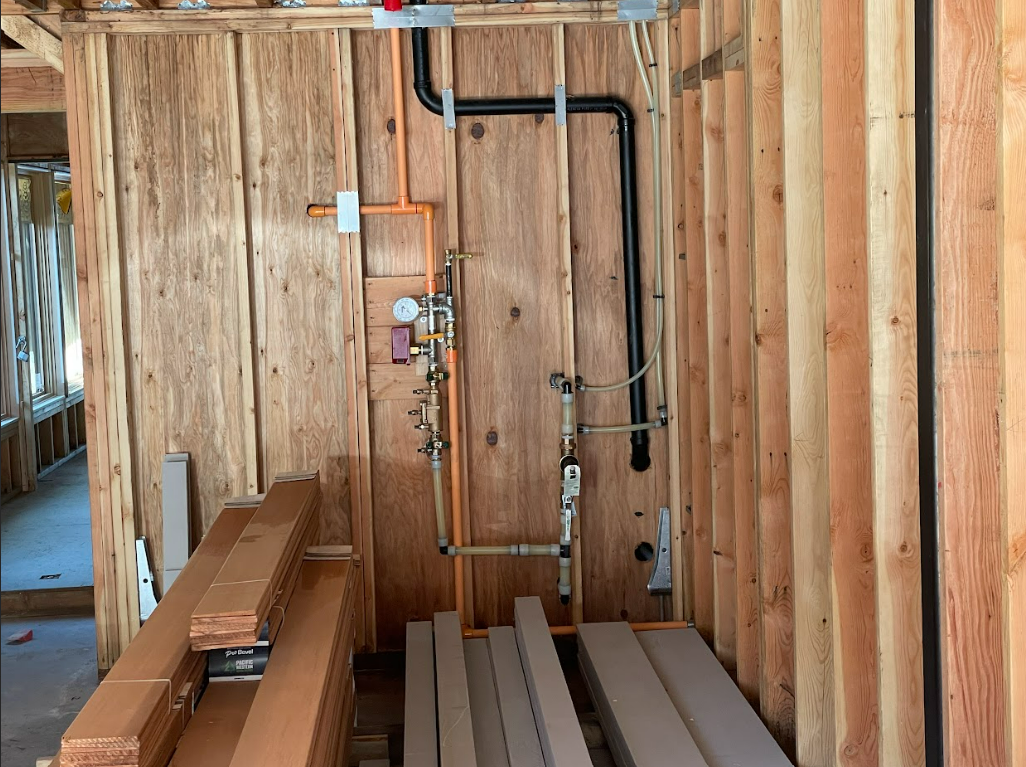 A room in a house under construction with wooden walls and pipes.