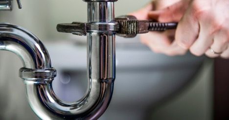 A plumber is fixing a sink pipe with a wrench.