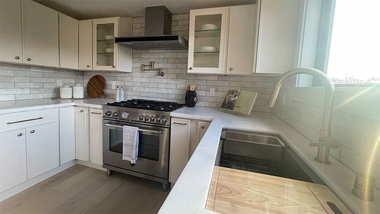A kitchen with white cabinets , stainless steel appliances , a sink and a stove.