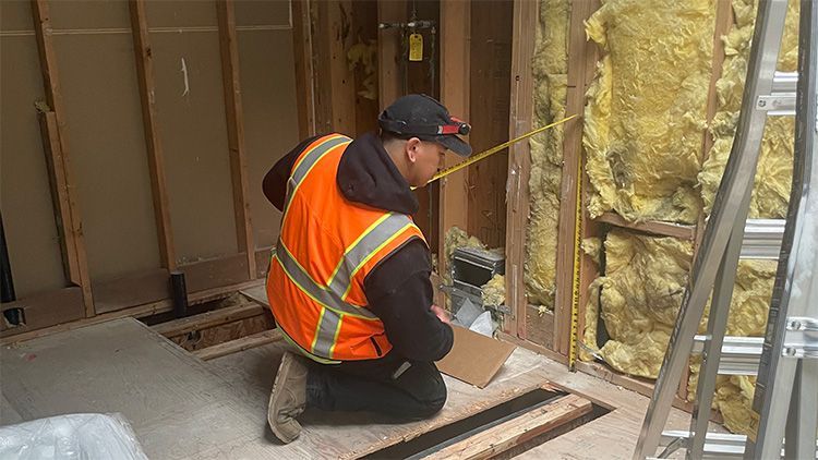 A construction worker is measuring a wall with a tape measure.