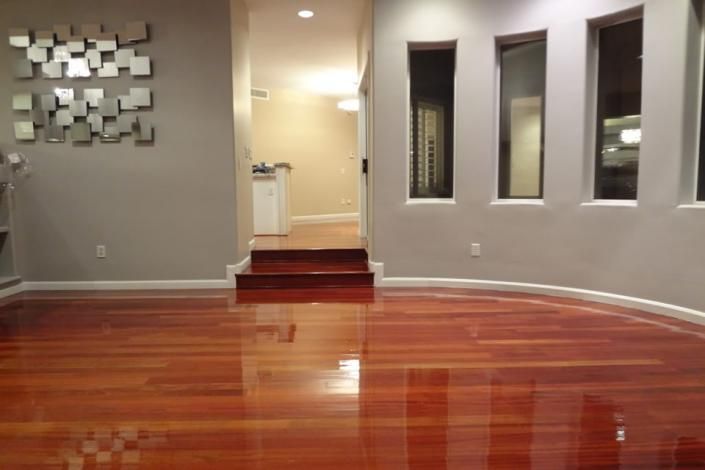 Empty room with glossy hardwood floor, gray walls, and a small step-up entryway with windows.