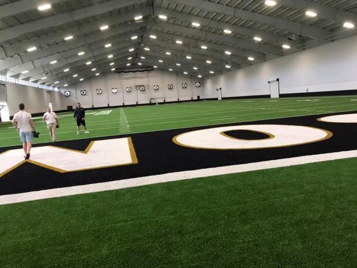 Indoor sports field with large black-and-gold letters and a few people walking on the turf