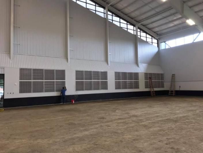 Empty indoor sports hall with high white walls, large windows, and a person standing near the wall