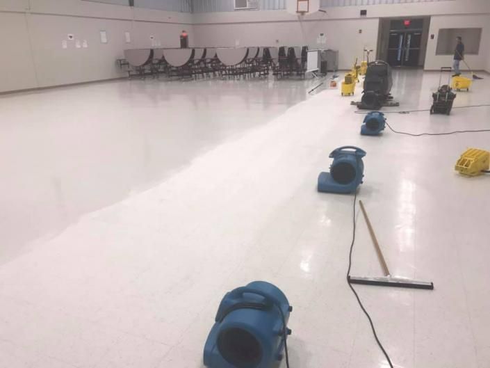 White indoor ice rink with blue floor dryers and a bench of people in the background