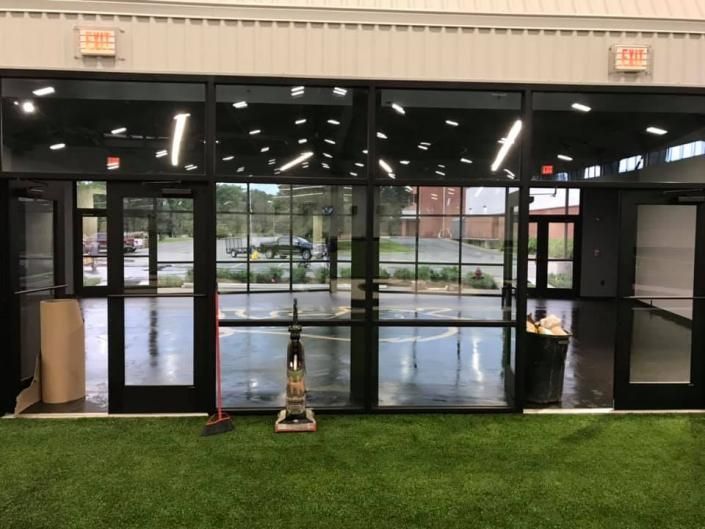 Empty storefront with glass doors, wet floor, and a small table on artificial grass inside.
