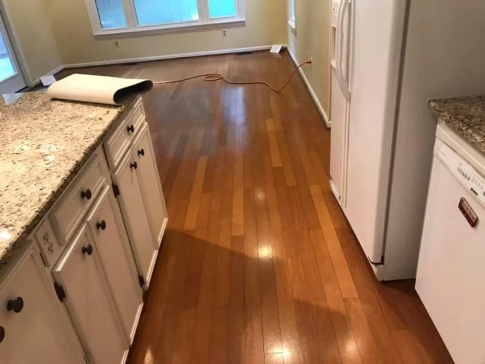 Empty kitchen with hardwood floor, white cabinets, granite countertops, and a rolled-up rug near the window.