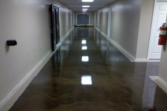 Empty hallway with glossy floor and bright reflections, viewed toward a distant doorway.