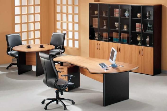 Modern office with empty desks, black chairs, and a wood cabinet against a warm grid-pattern wall.
