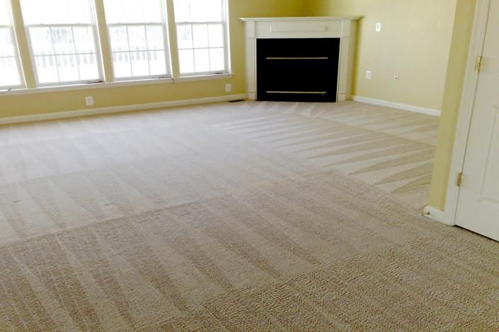 Empty beige carpeted room with large windows and a fireplace.