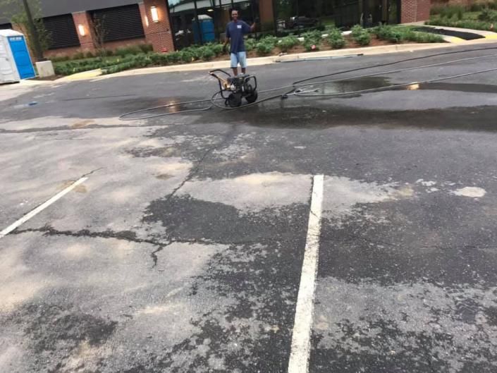 Person on a wheelchair/scooter crossing a wet parking lot near a brick building.
